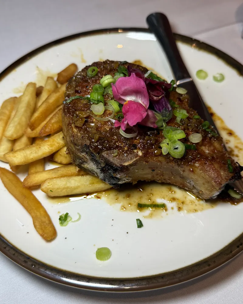 Bone-in chop topped with scallions and edible flowers, served with fries