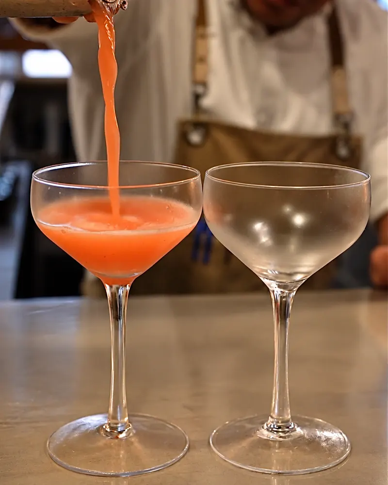 Bartender straining a pink cocktail into a coupe glass
