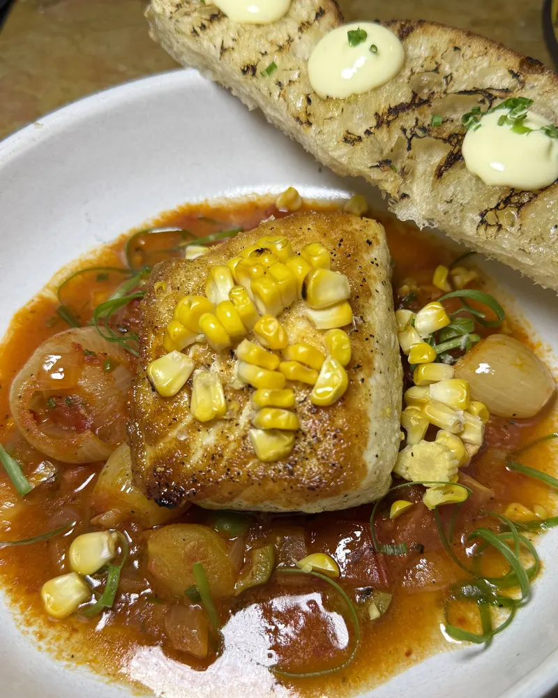 Seared fish fillet with charred corn in a tomato broth, served with grilled bread
