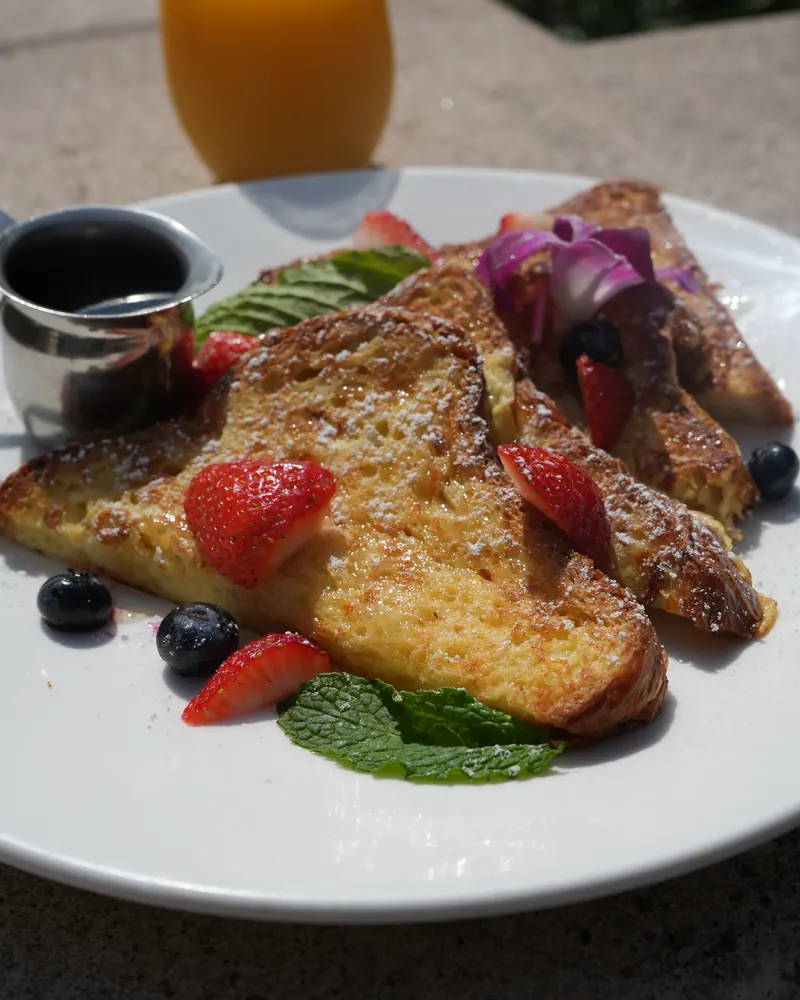 French toast with powdered sugar, strawberries, blueberries and mint, with a glass of orange juice
