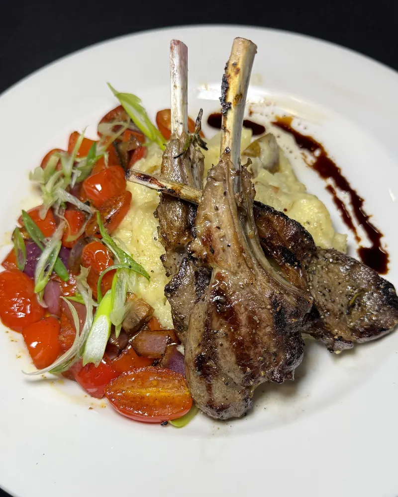 Grilled lamb chops over mashed potatoes with blistered tomatoes and scallions