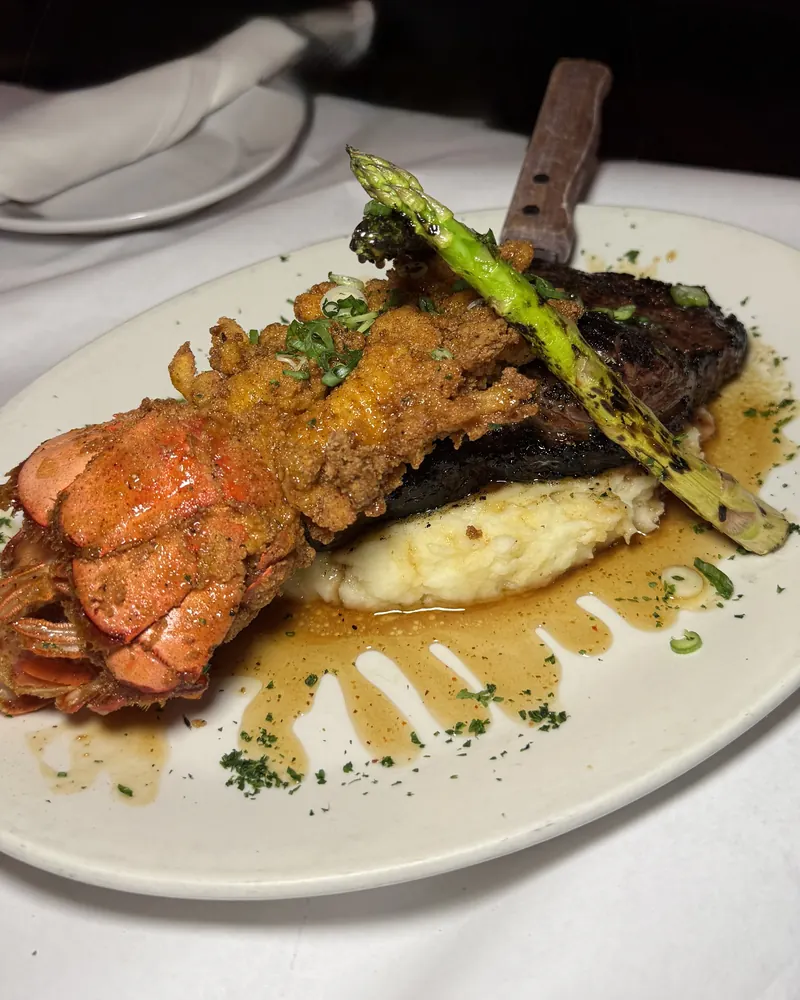 Steak and fried lobster tail over mashed potatoes with grilled asparagus